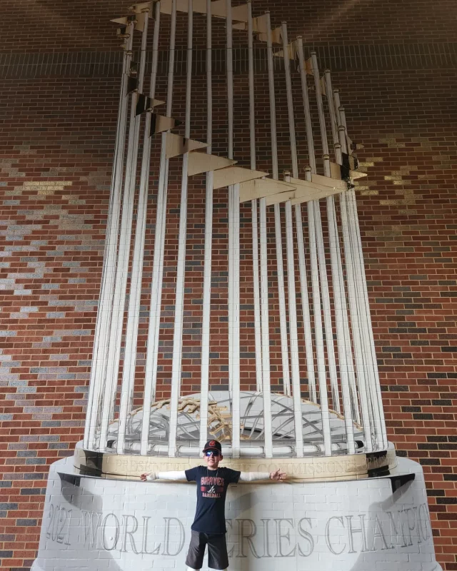moments of joy | Epidermolysis Bullosa News | Jonah stands with his arms spread wide before a massive wall painting of the 2021 MLB World Series trophy, won by the Braves