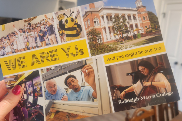 A photo of a woman's hand holding an advertising flyer for a college called Randolph-Macon College. Black text over a yellow background reads, "We are YJs," and, "And you might be one, too." It has various photos from life around campus, with a bumble bee mascot and theme. 